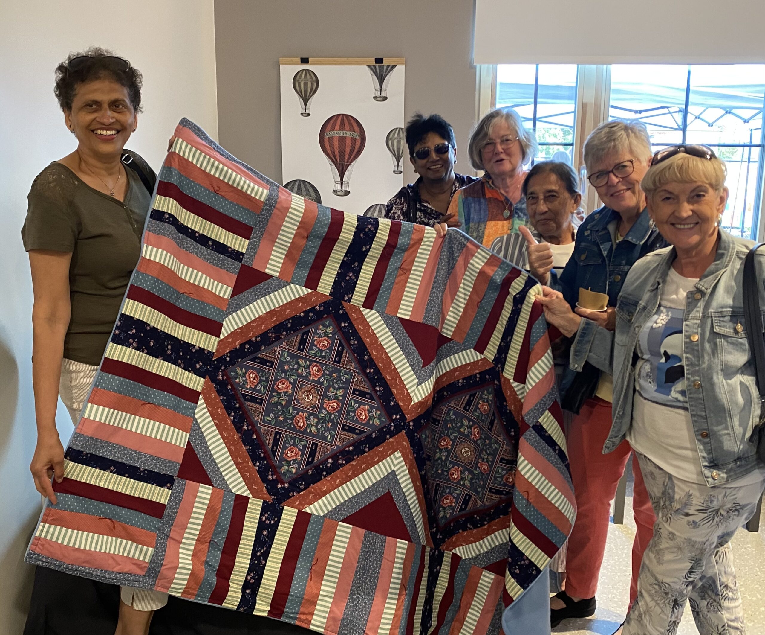 Women holding up a quilt they made together.